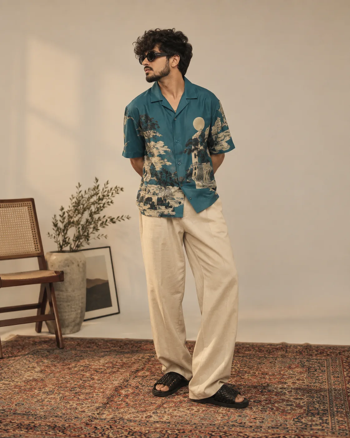 Full-body studio fashion portrait of a man standing on an ornate patterned rug in a minimalist studio.