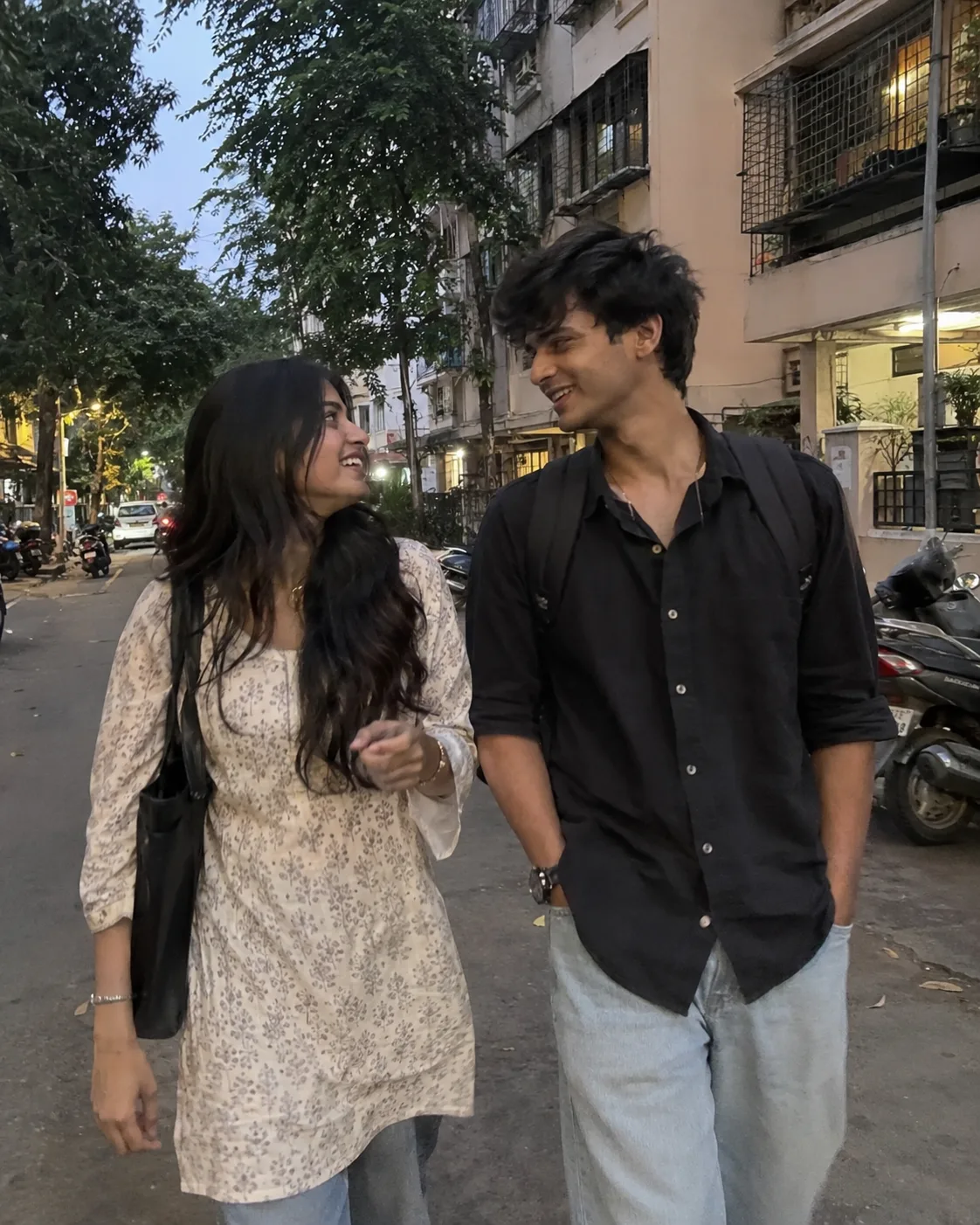 Photorealistic 4:5 vertical iPhone photo of a young Indian couple casually walking together on a normal Mumbai residential street in the