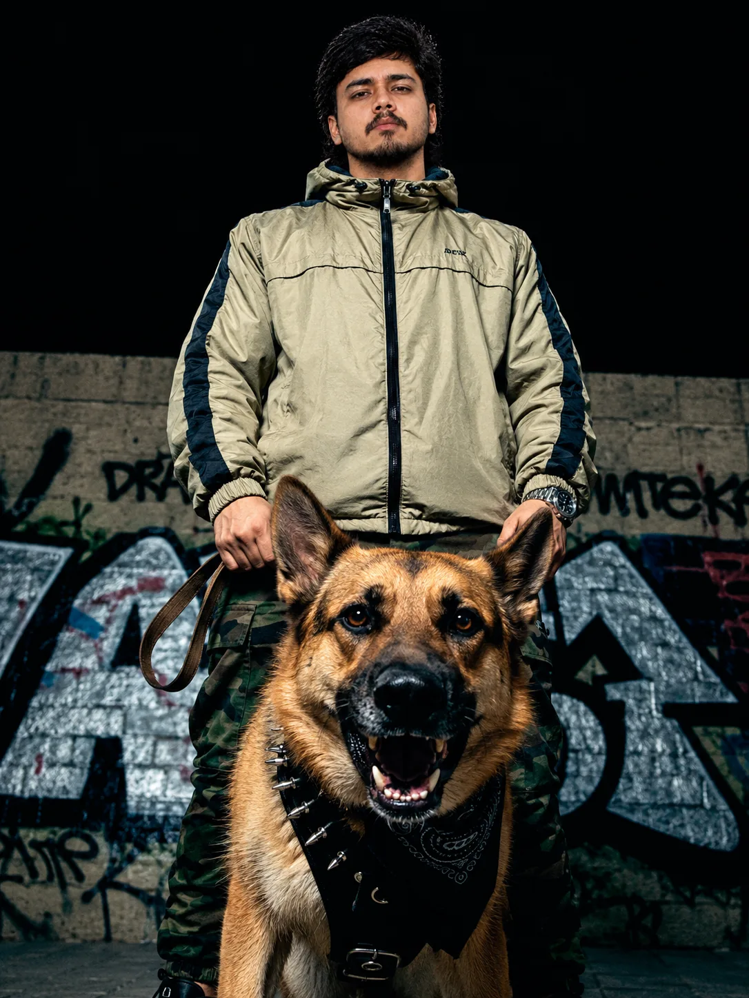 A photorealistic cinematic portrait of a young adult man standing confidently at night in front of a rugged concrete wall covered with bold