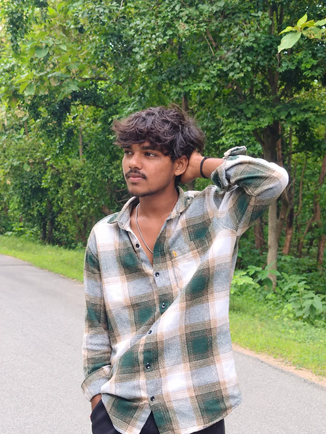 Ultra-realistic cinematic outdoor portrait of a young Indian man standing casually on a quiet forest road, surrounded by dense lush green