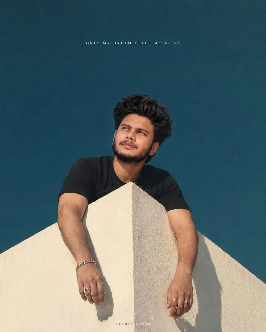 Prompt: Cinematic portrait of a young South Asian man with wavy dark hair and a short beard, looking upward with a calm, dreamy expression.