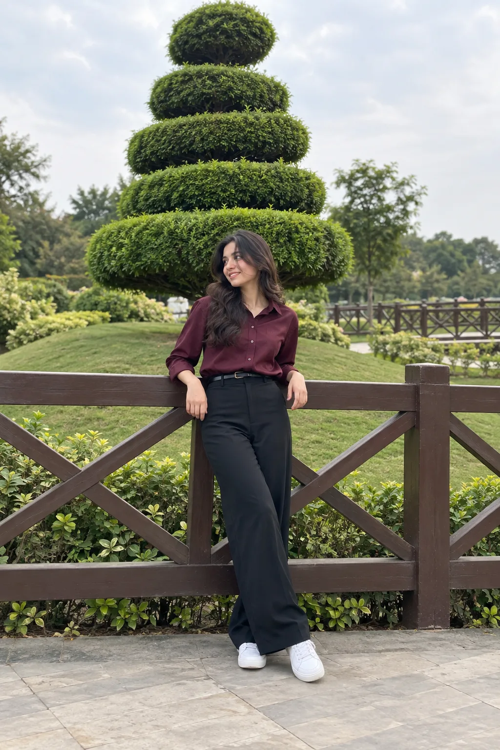 A full-shot aesthetic photograph of a young woman with natural wavy dark hair, wearing a dark plum-maroon button-down collared shirt and