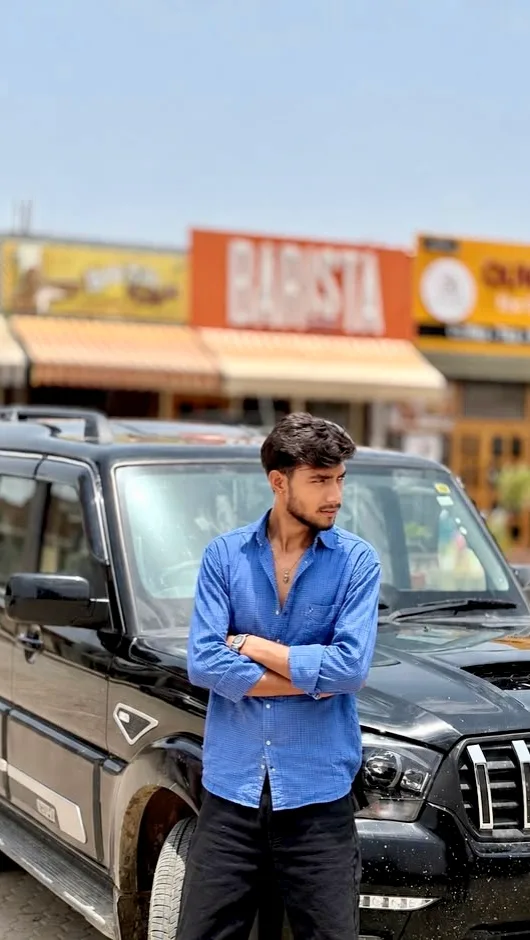 A photorealistic vertical medium shot of the young South Asian man from the reference image, faithfully preserving his exact recognizable