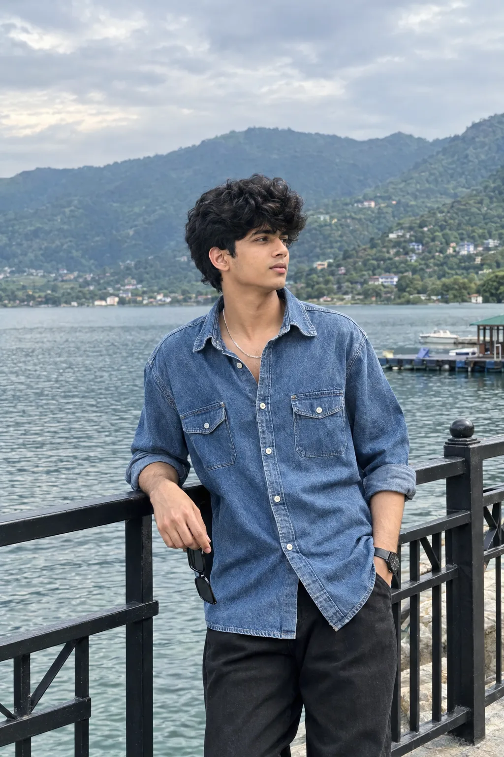 Create a premium, ultra-photorealistic luxury travel-fashion portrait of a young South Asian male standing beside a serene mountain lake on