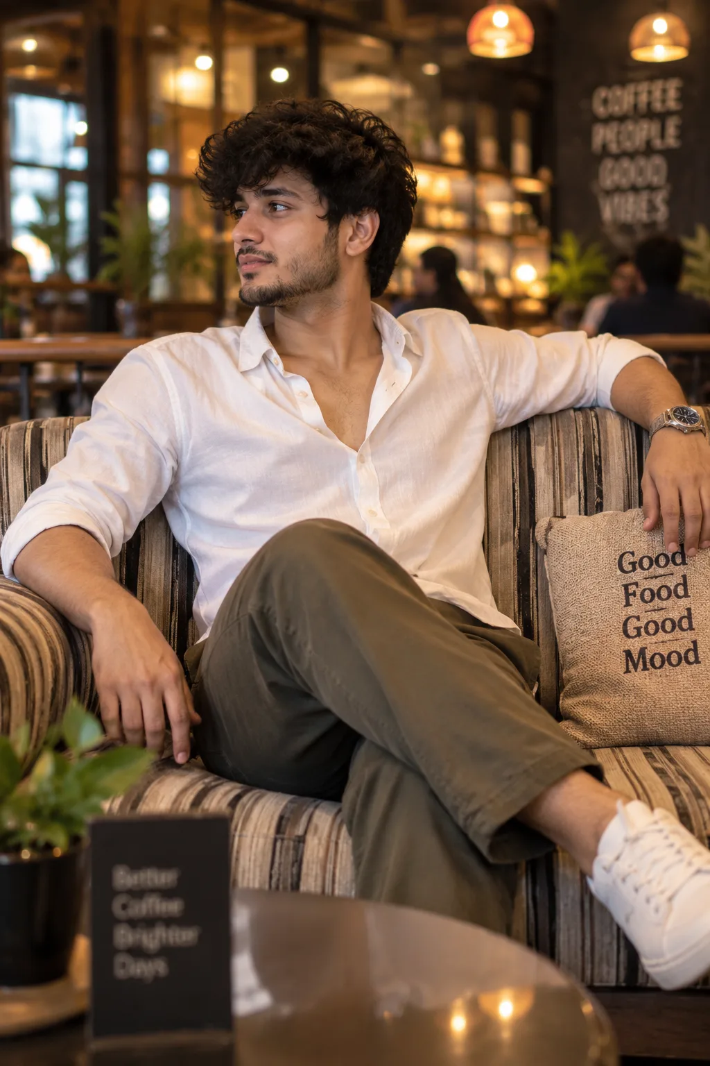 Relaxed café portrait of a young man seated on a striped sofa, leaning back with left arm resting on the backrest and right hand relaxed on