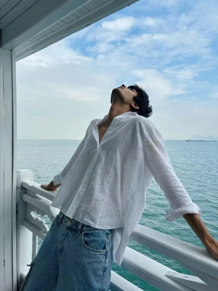 Ultra-realistic cinematic fashion photograph of a young male standing on a white seaside balcony, wearing a loose oversized white linen