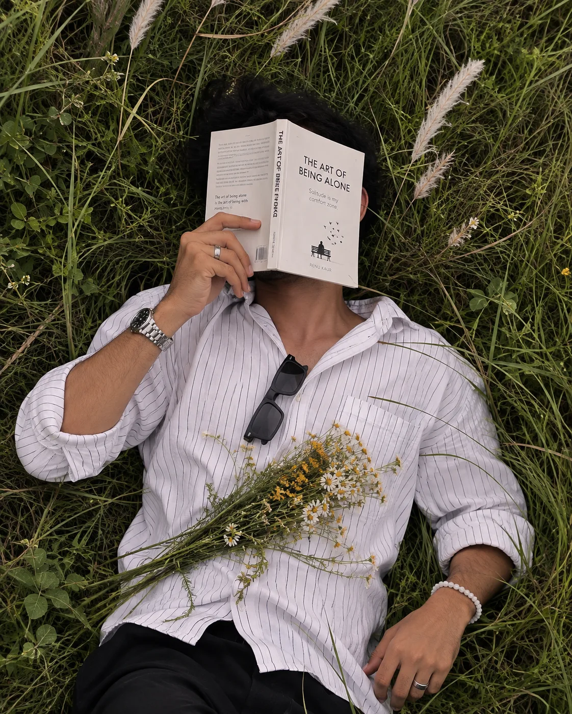 Create an ultra-realistic overhead lifestyle photograph of a handsome young South Indian man lying peacefully on his back in a dense field