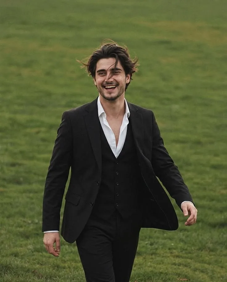 A candid medium shot of a handsome young man with messy, wind-blown dark brown hair, laughing joyfully.