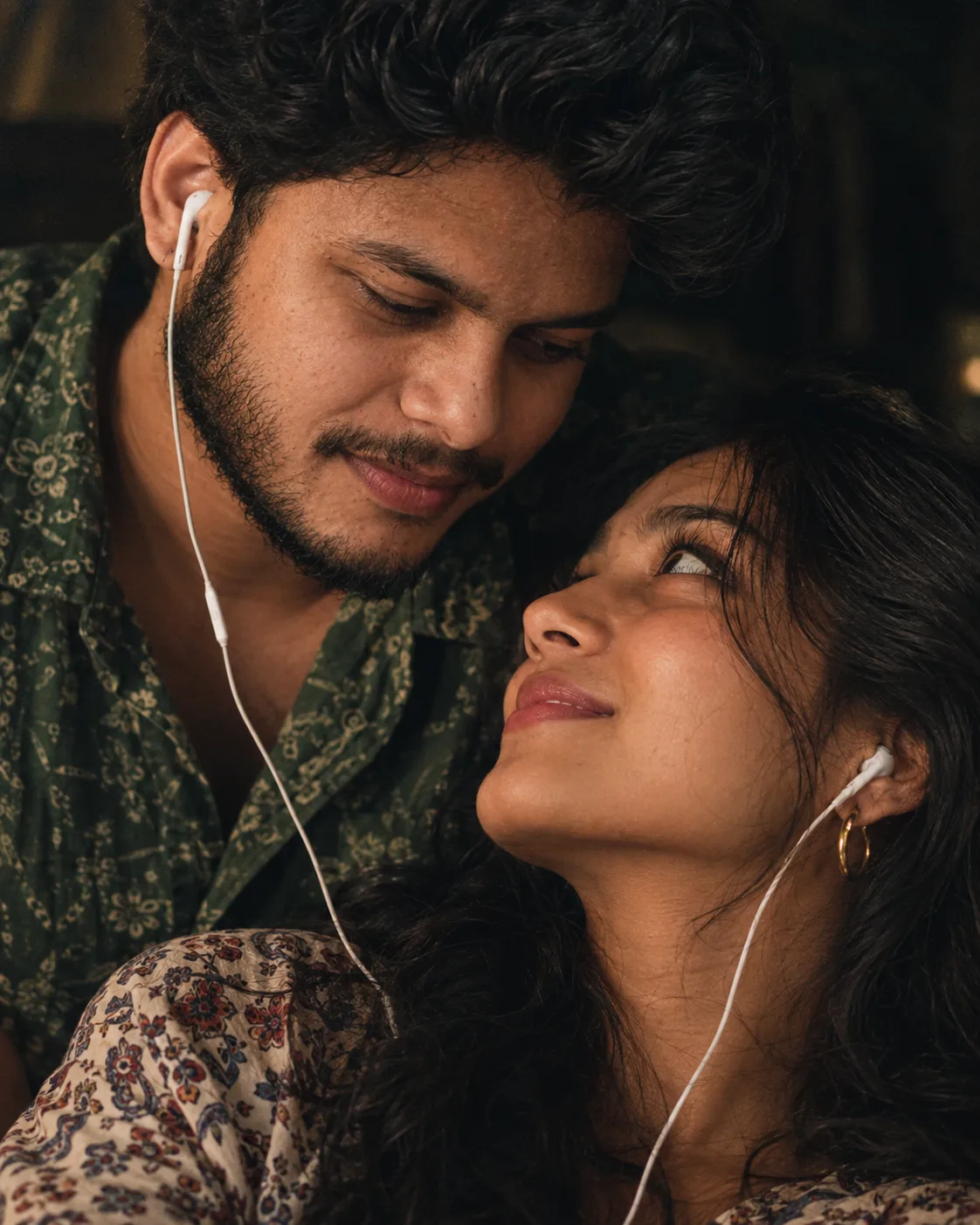 Create an ultra-realistic, intimate cinematic close-up portrait of a young South Asian couple sharing wired white earphones and listening