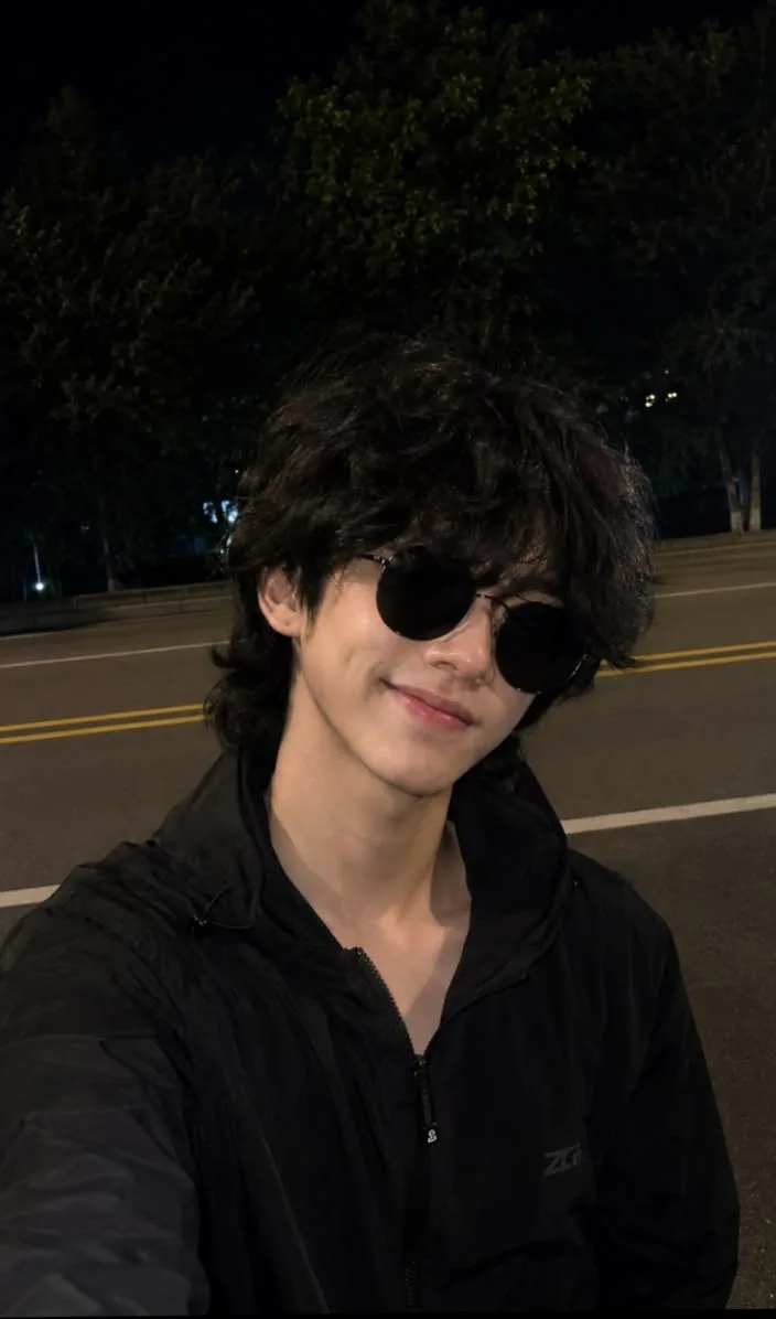 An ultra-realistic luxury night-time streetwear editorial portrait of a stylish young male model taking a casual selfie on an empty city
