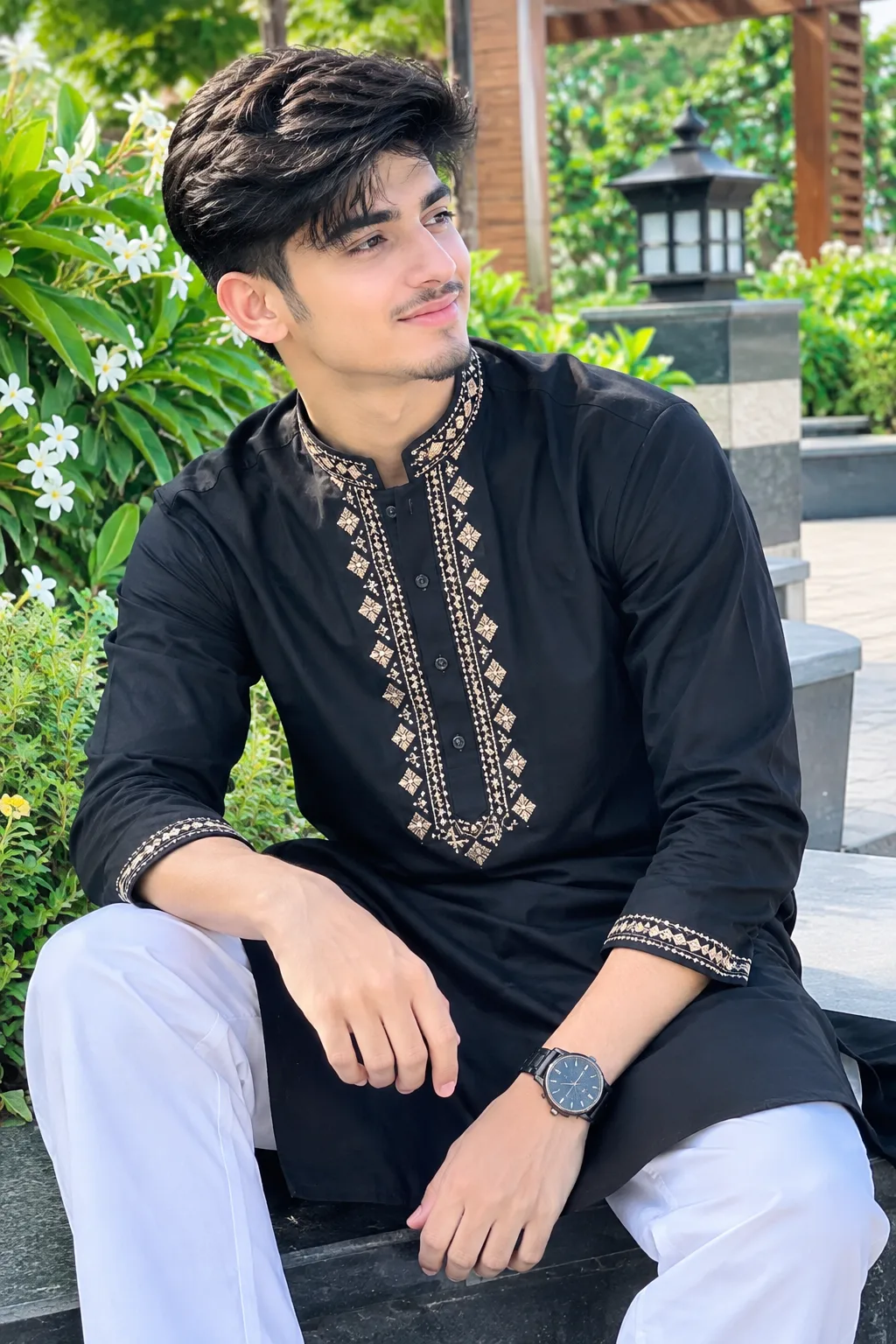 A handsome young South Asian male model wearing a stylish black embroidered kurta with cream-gold detailing, white trousers, and a luxury