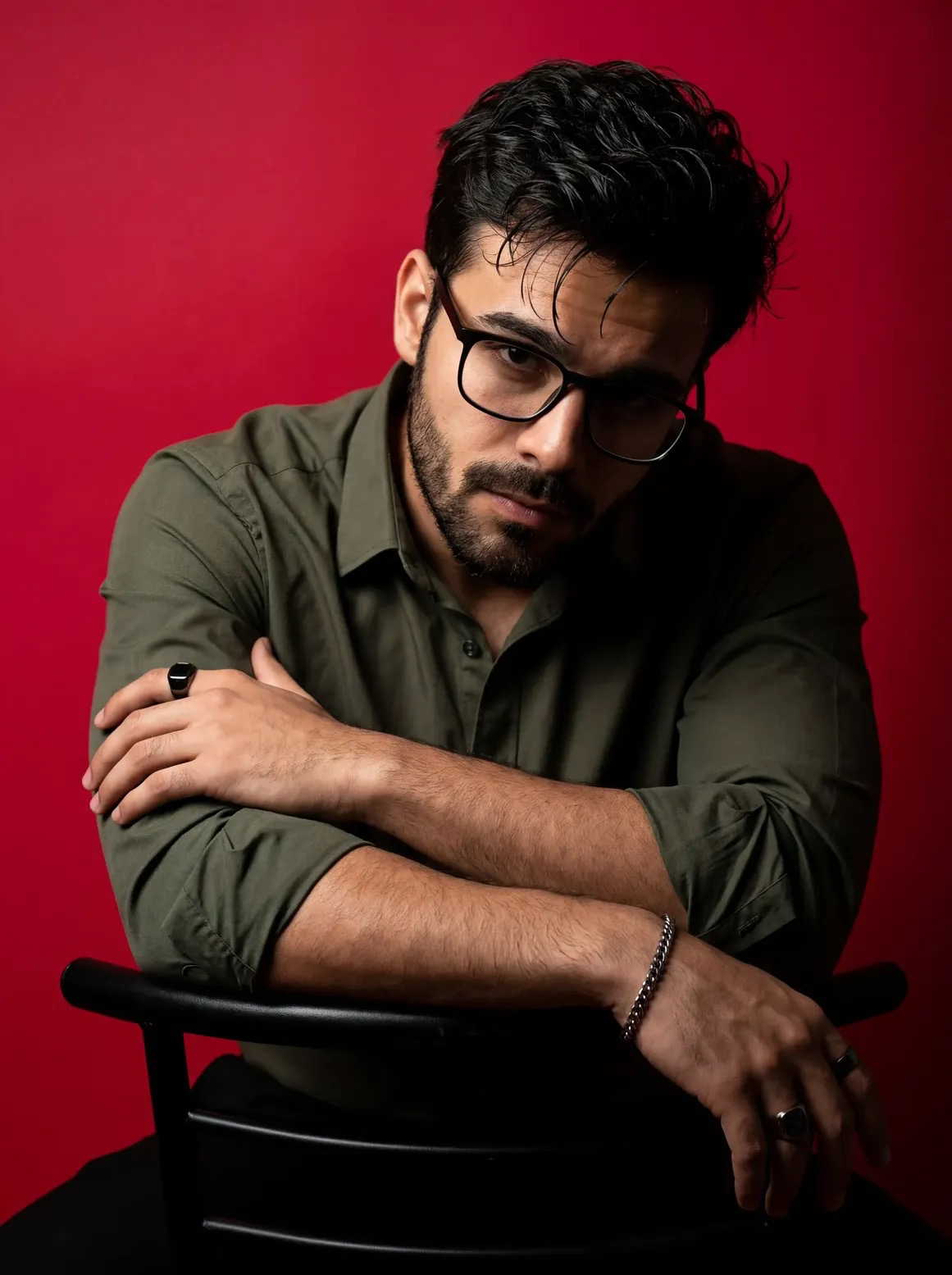 A dramatic, high-contrast studio portrait of a man with dark messy hair and a well groomed beard, wearing black rectangular glasses and a