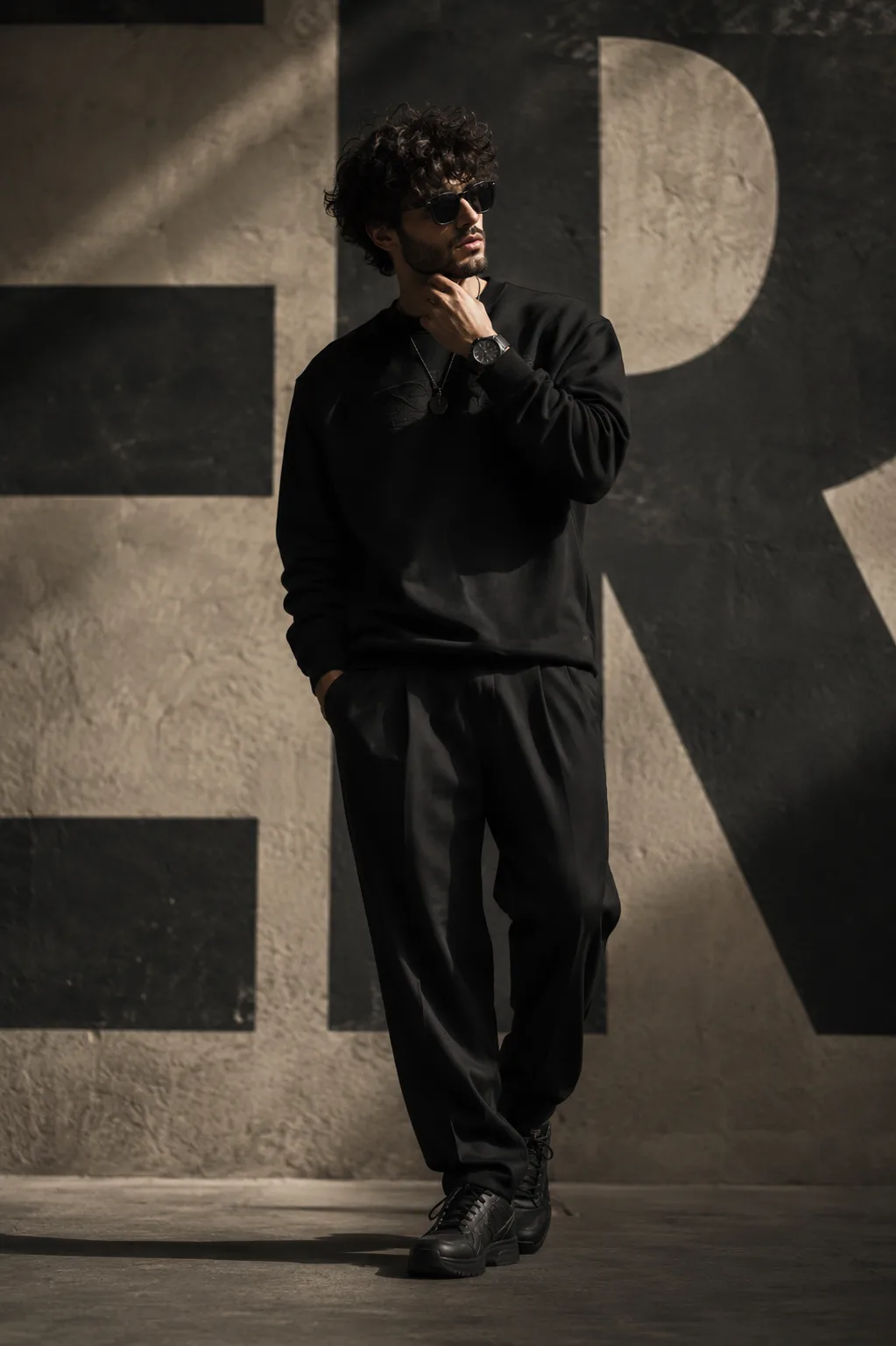 A breathtakingly charismatic young male fashion model standing confidently against a bold minimalist urban backdrop featuring oversized