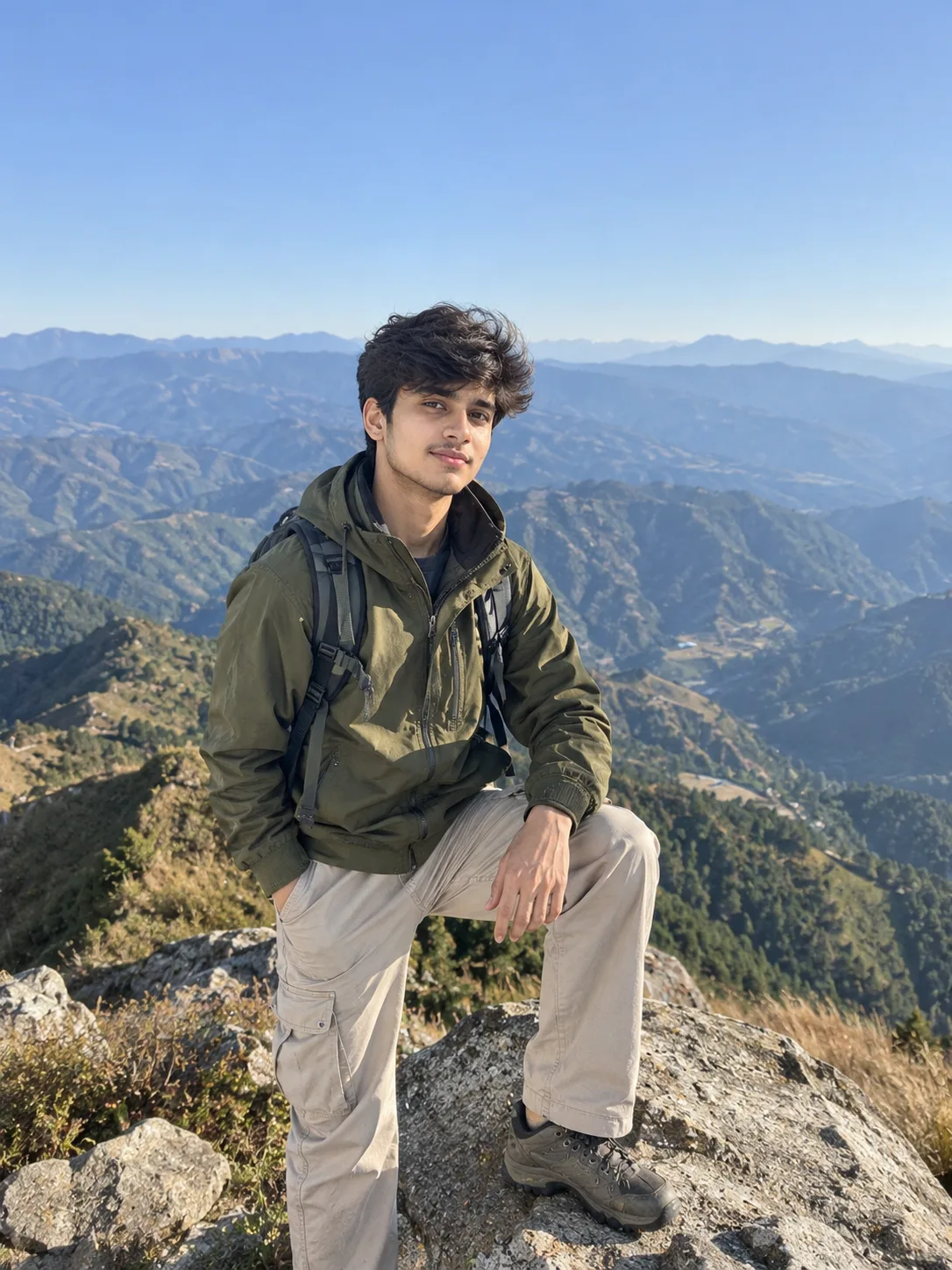 Ultra realistic photograph of a young man standing on a mountain peak during daytime, shot on a real DSLR camera.