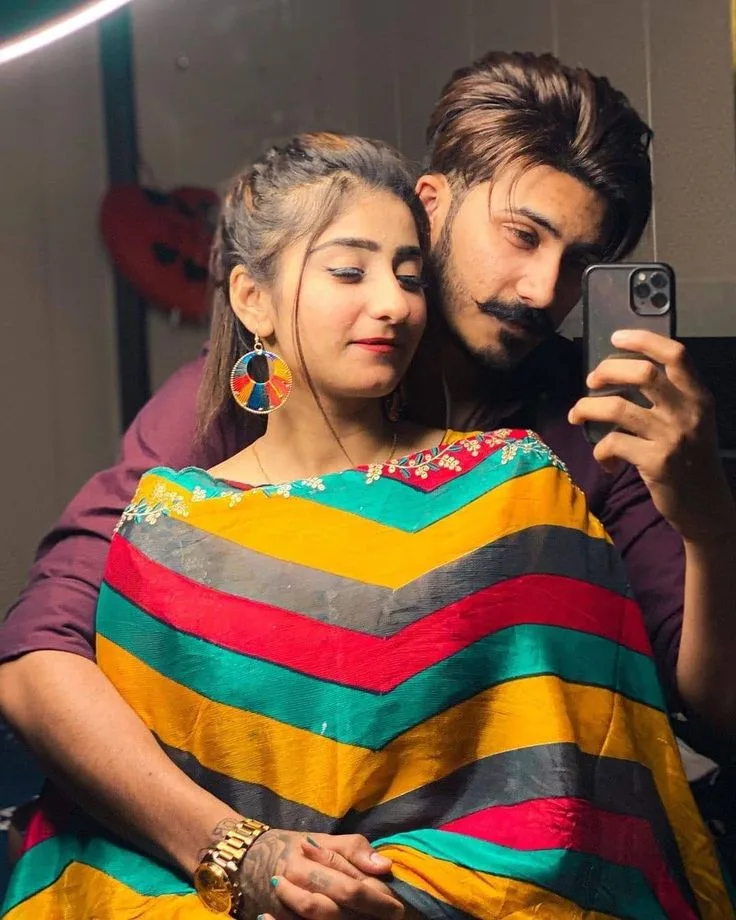 A photorealistic vertical medium close-up shot capturing an intimate candid mirror selfie of the young South Asian couple from the