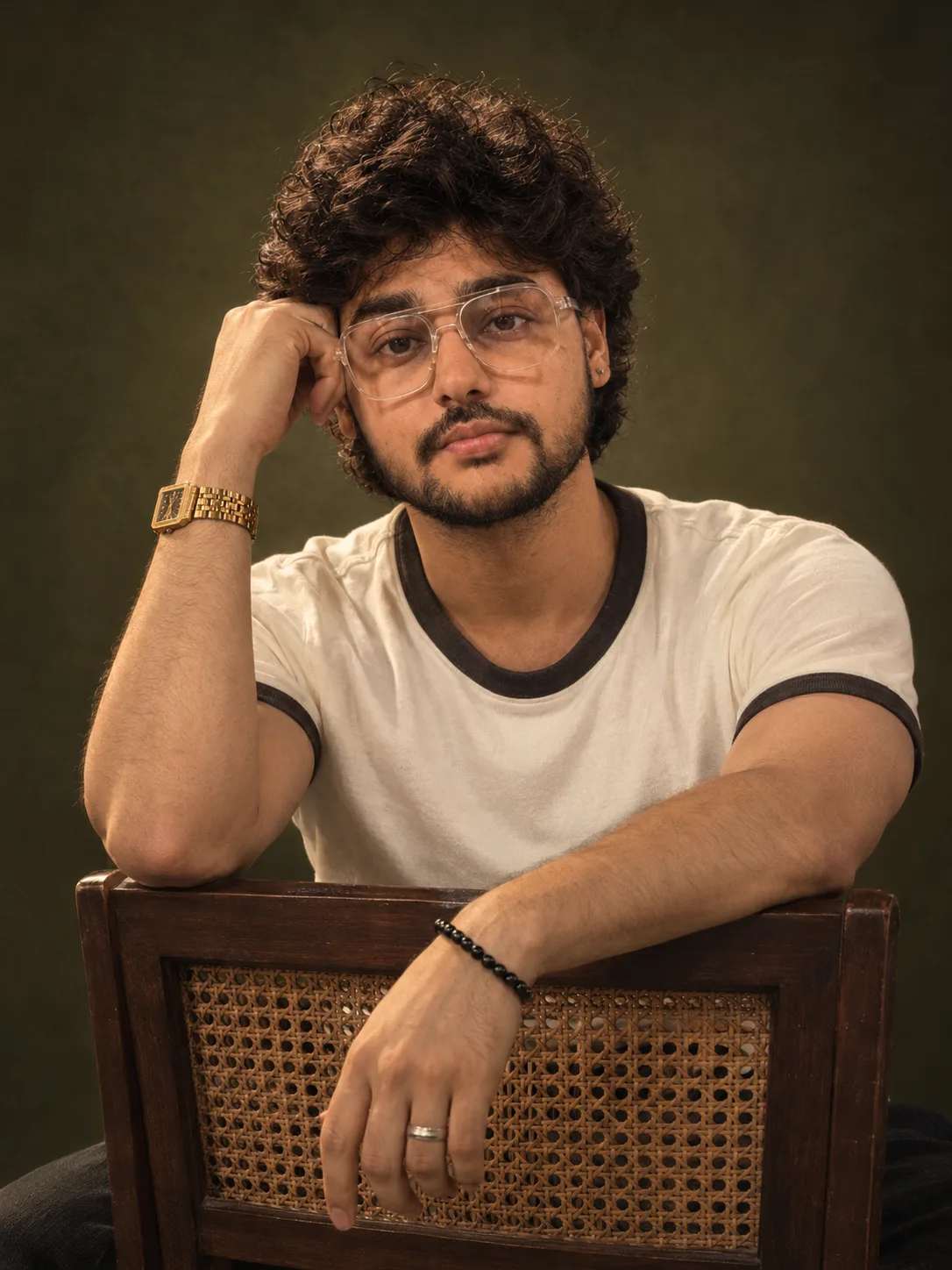 "A polished studio portrait of a young man with thick, soft, tousled black curly hair falling loosely over his forehead, looking at the