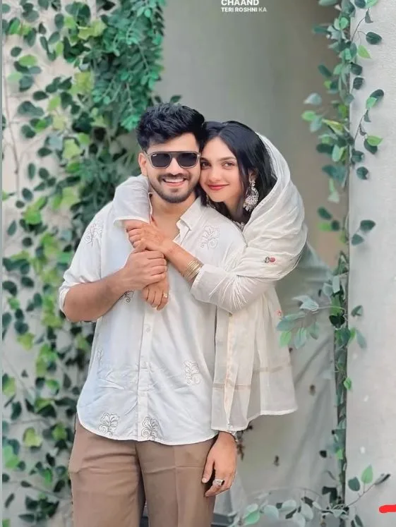 A photorealistic vertical medium shot of the young South Asian couple from the reference image, faithfully preserving both subjects' exact