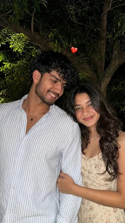 Create an ultra-realistic candid night-time portrait of a young couple standing closely together outdoors in a natural garden setting.