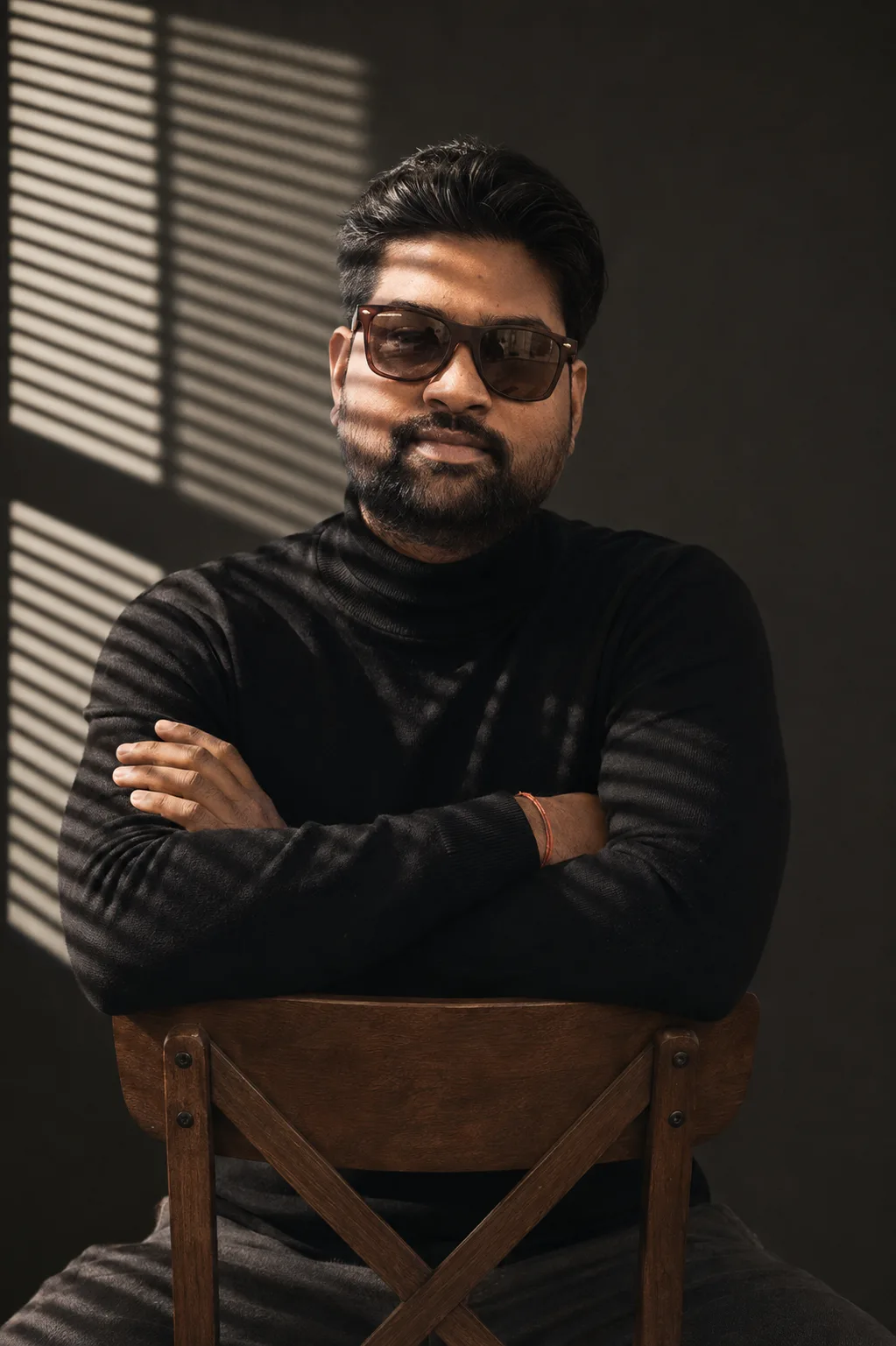 A cinematic moody portrait of a young South Asian man with a neat beard, wearing dark tinted stylish sunglasses and a black fitted