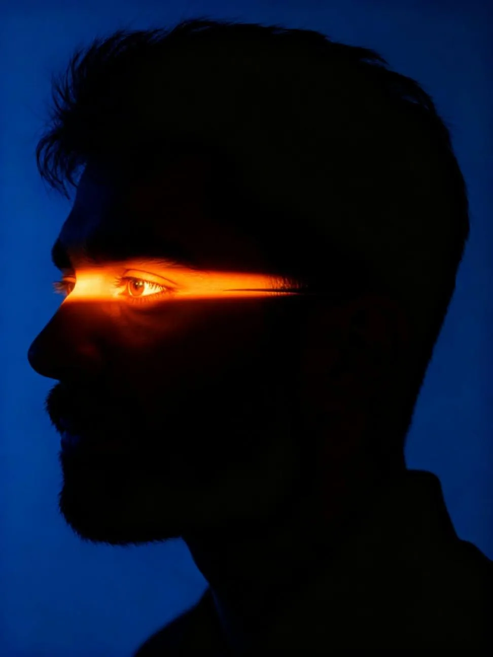 "Cinematic low-key portrait of a man in profile, dramatic chiaroscuro lighting, deep blue ambient shadows, a sharp horizontal slit of
