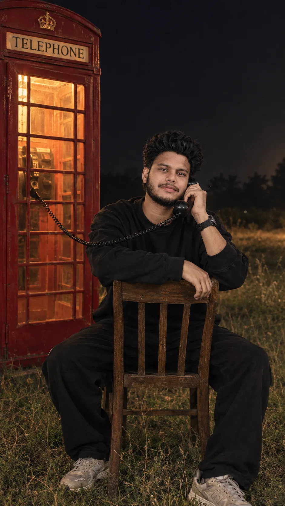 Create an ultra-photorealistic cinematic night photograph of a young South Asian man sitting backwards on a vintage wooden chair in a