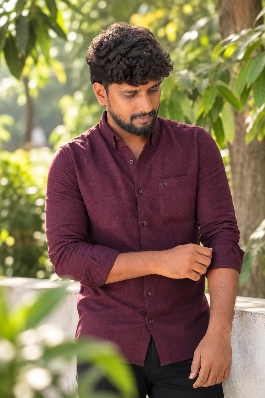 Create a highly realistic professional outdoor portrait of a young South Asian man wearing a premium deep maroon button-down shirt with the