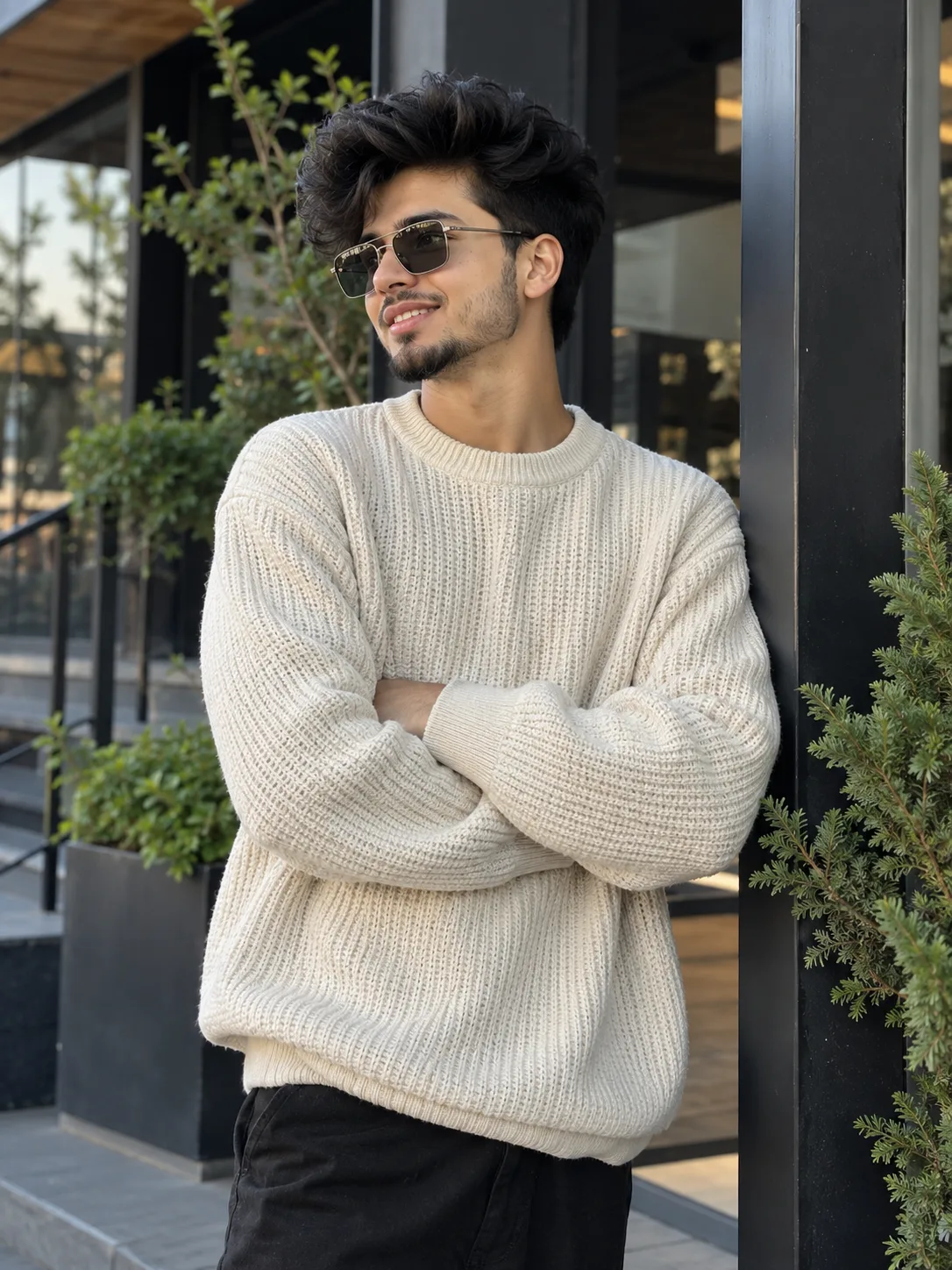 Ultra realistic photograph of a handsome young Indian man posing casually in a modern outdoor setting, wearing a textured oversized