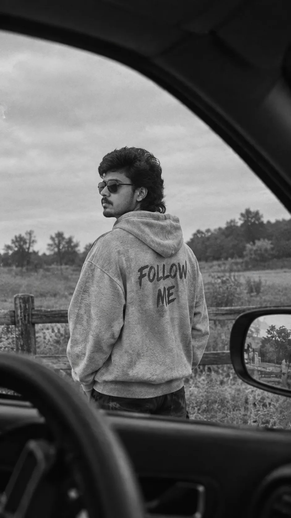 Ultra-realistic black and white cinematic photo of me standing outside near a wooden fence in an open rural area, viewed from inside a