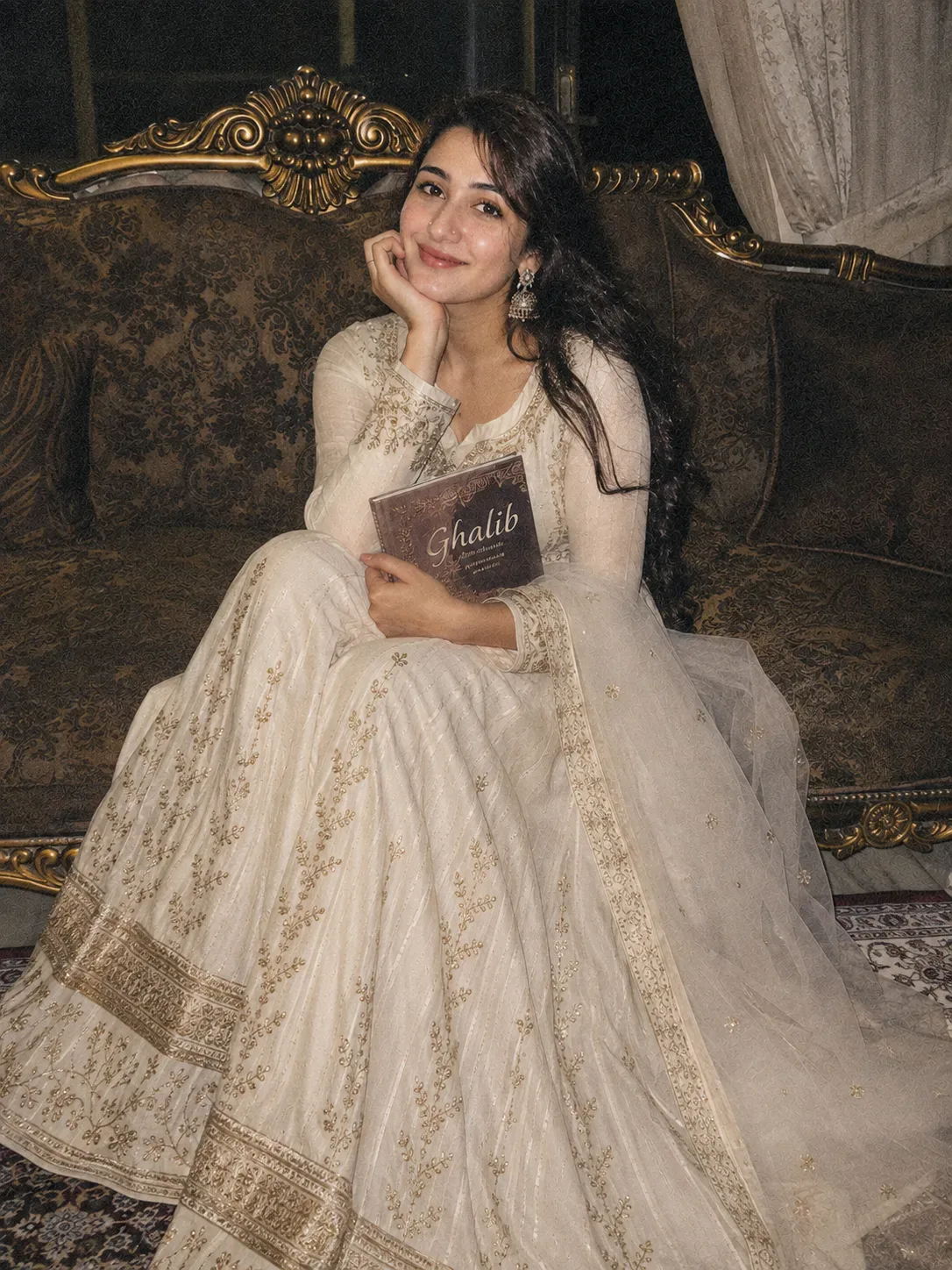 Same person as the reference image, same identity, I'm sitting on a royal sofa, smiling while looking at the camera, a book named "ghalib "