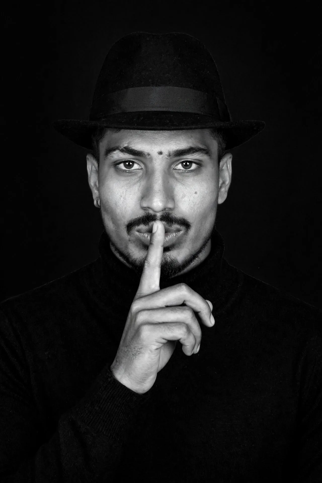 A high-quality, black and white fine art portrait of a sophisticated man wearing a classic black wool fedora with a grosgrain ribbon, a