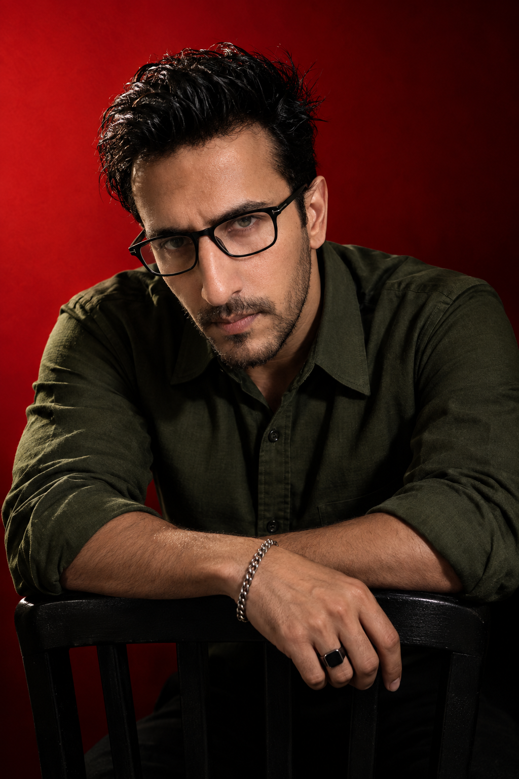 A dramatic, high-contrast studio portrait of a man with dark messy hair and a well groomed beard, wearing black rectangular glasses and a