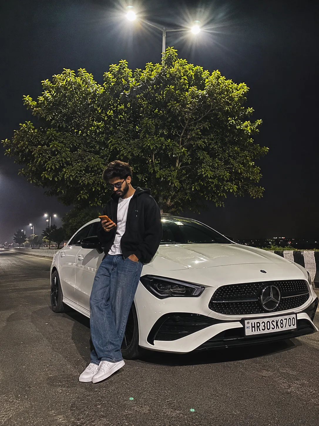Photorealistic cinematic night street photo, a young bearded man with stylish hair and light beard, black oversized hooded jacket, white