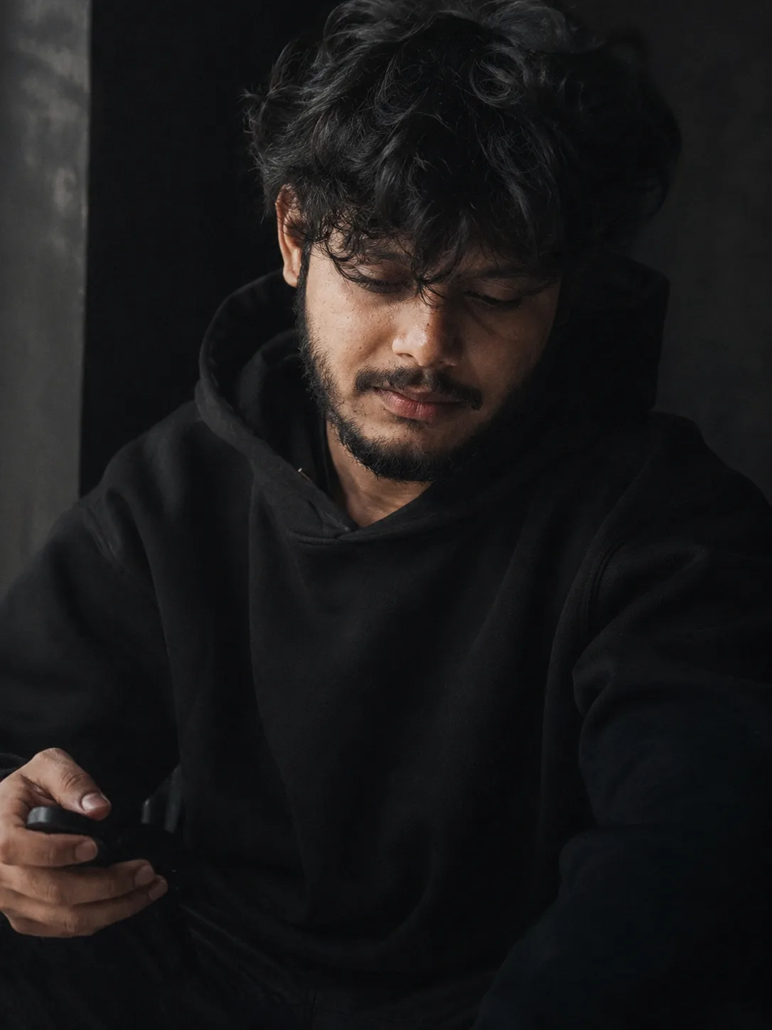 A cinematic, moody medium-close-up portrait of a 26-year-old south Asian man with expressive dark eyes, medium-length messy curly hair