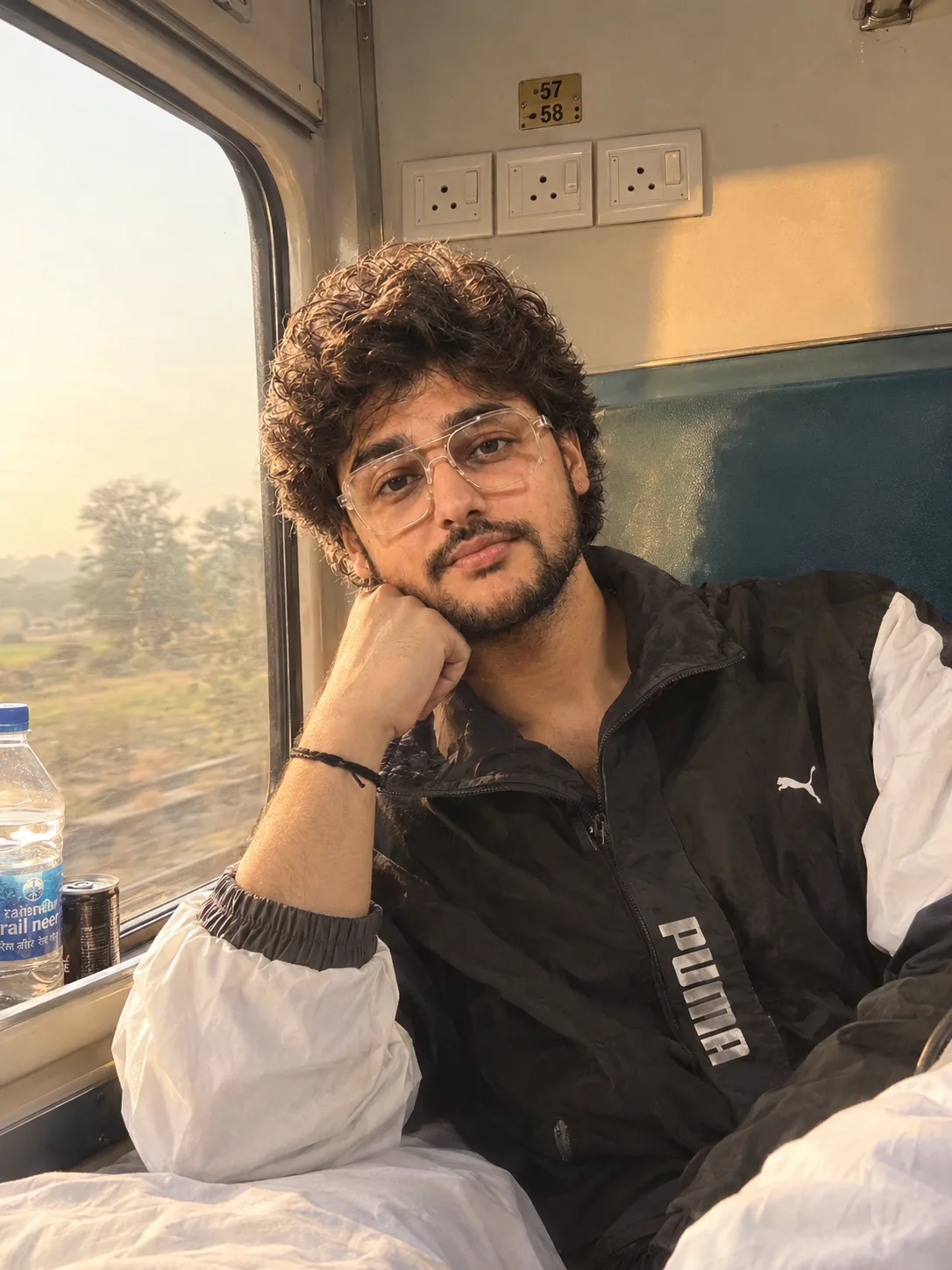 "A candid lifestyle portrait of a young man with thick, curly dark brown hair and a full, neatly trimmed black beard and mustache, looking