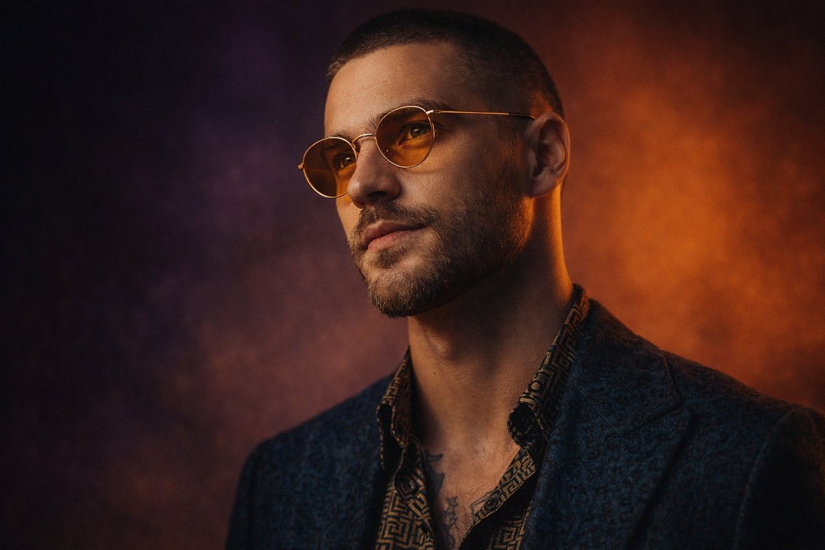 Ultra-realistic studio portrait of a stylish man with a close buzz cut and neatly trimmed beard, wearing round amber-tinted glasses with