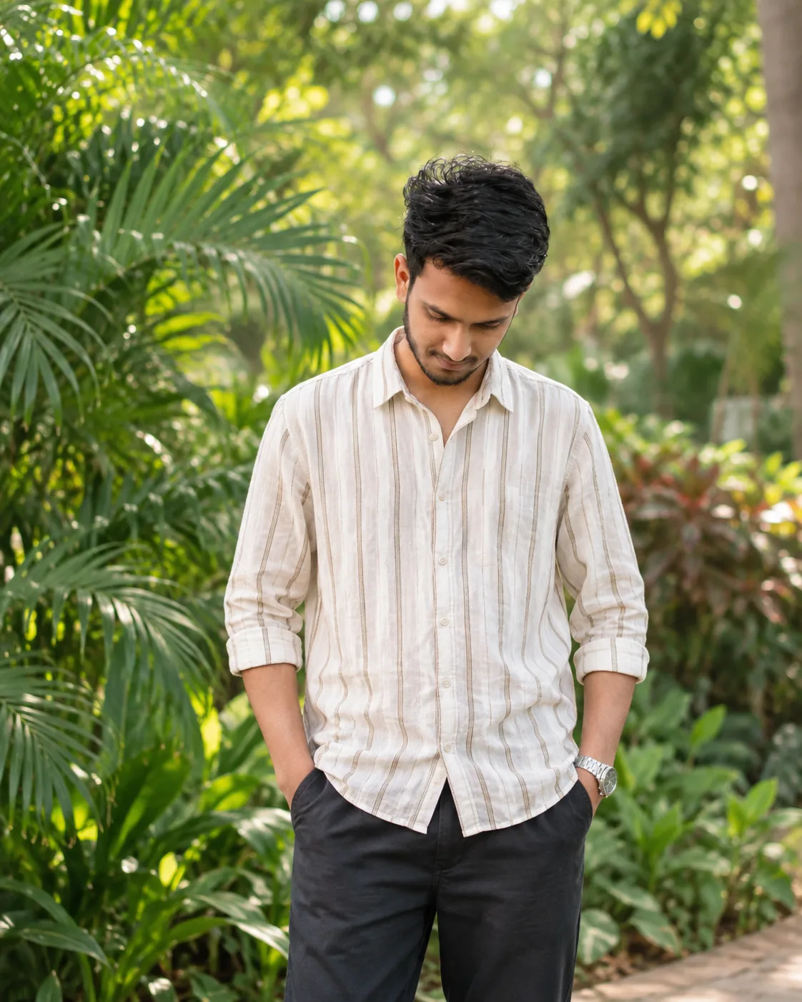 Create a highly realistic, ultra-detailed cinematic outdoor fashion portrait of a young Indian man standing casually in a lush green garden