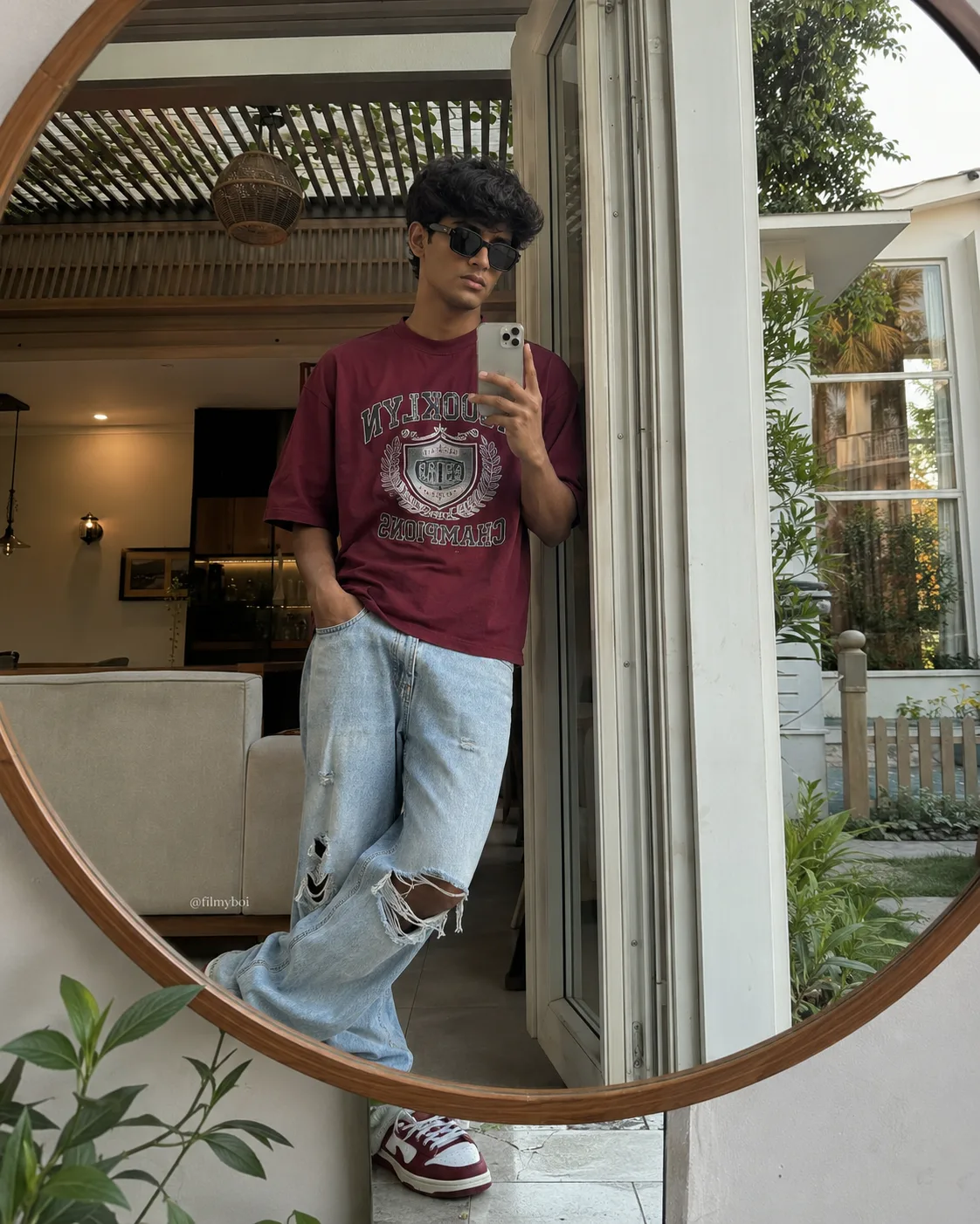 A 4:5 vertical, ultra-realistic photograph capturing a stylish young man taking a casual mirror selfie in a large circular mirror within a