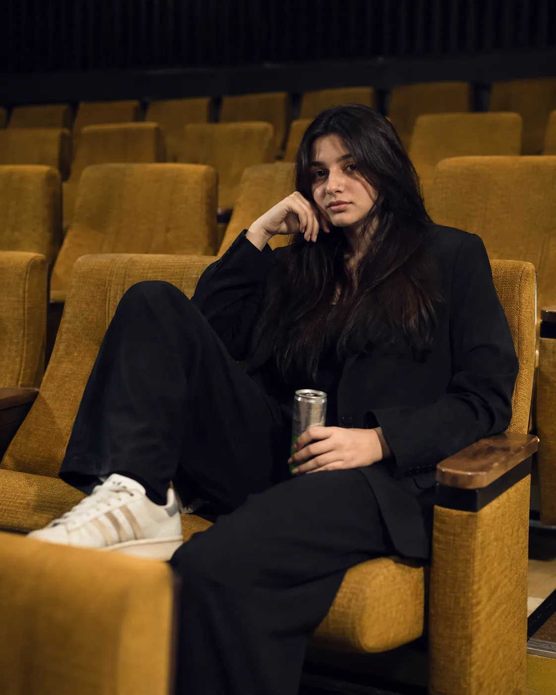 A medium shot portrait captures a young woman sitting in an empty movie theater or auditorium.