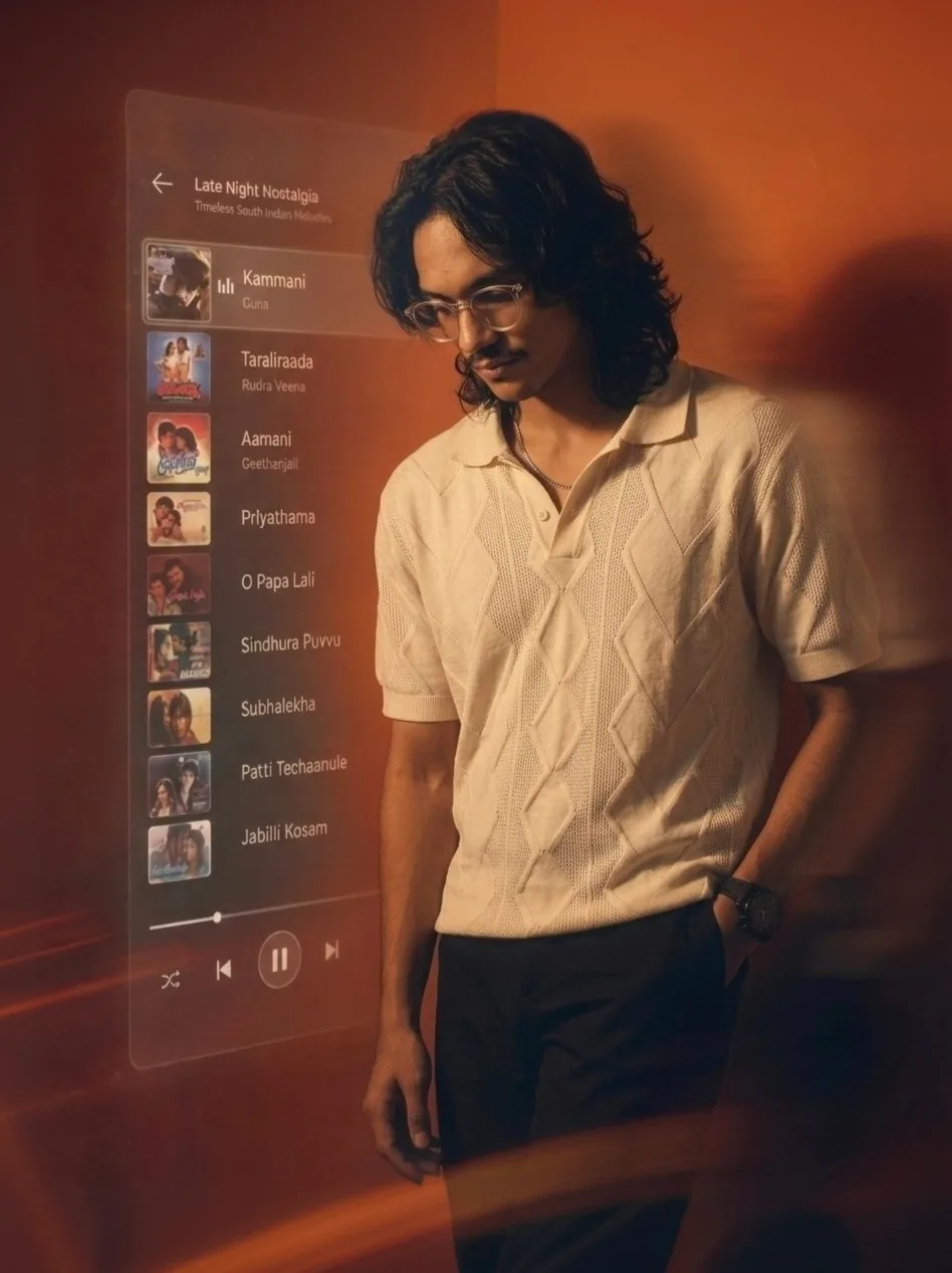 Ultra-realistic cinematic portrait of a stylish young South Indian man standing indoors in warm, moody amber lighting.