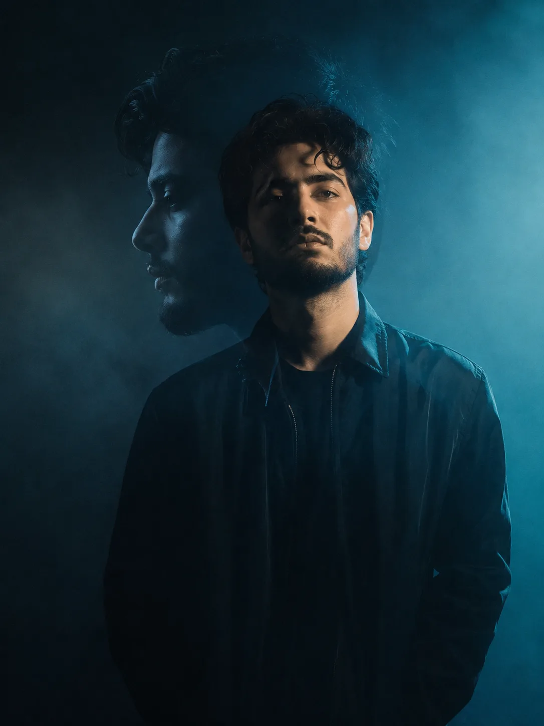moody cinematic portrait of a man in dark jacket, front facing but slightly turned, minimal expression, dark teal and cyan studio lighting,