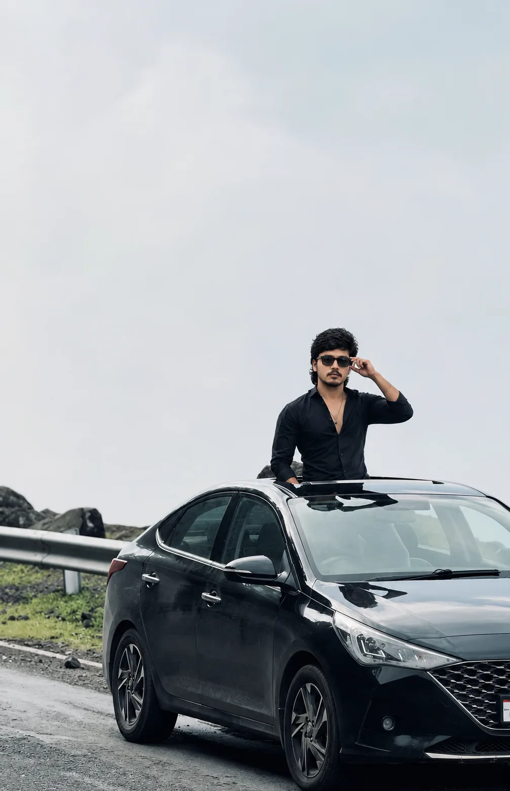 Create a photorealistic cinematic full-body portrait of a young Indian man standing through the open sunroof of a sleek black sedan parked