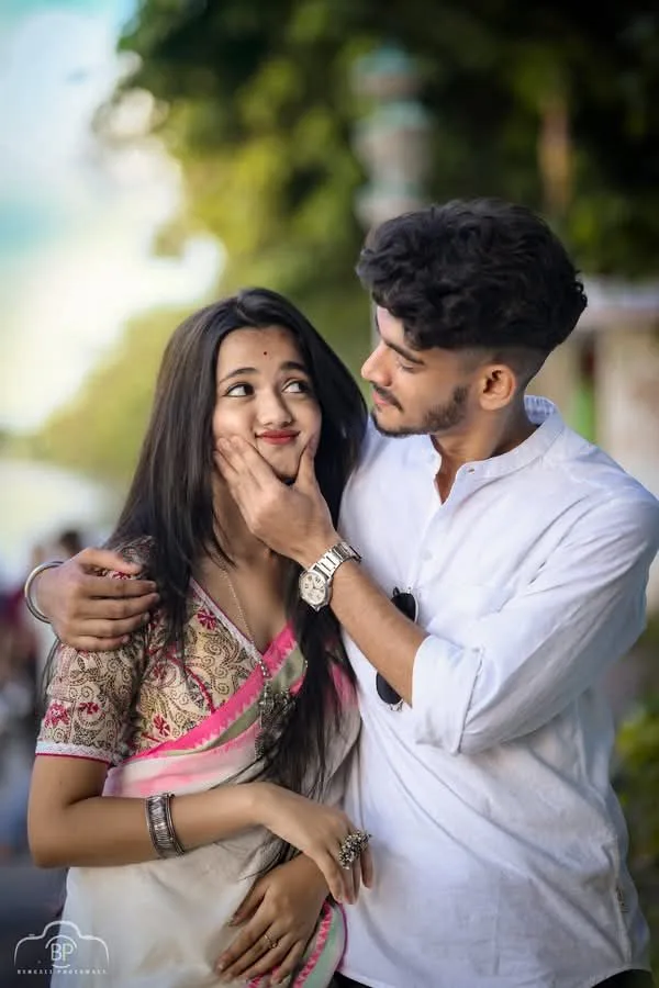 A photorealistic vertical medium shot of the young South Asian couple from the reference image, faithfully preserving both subjects' exact