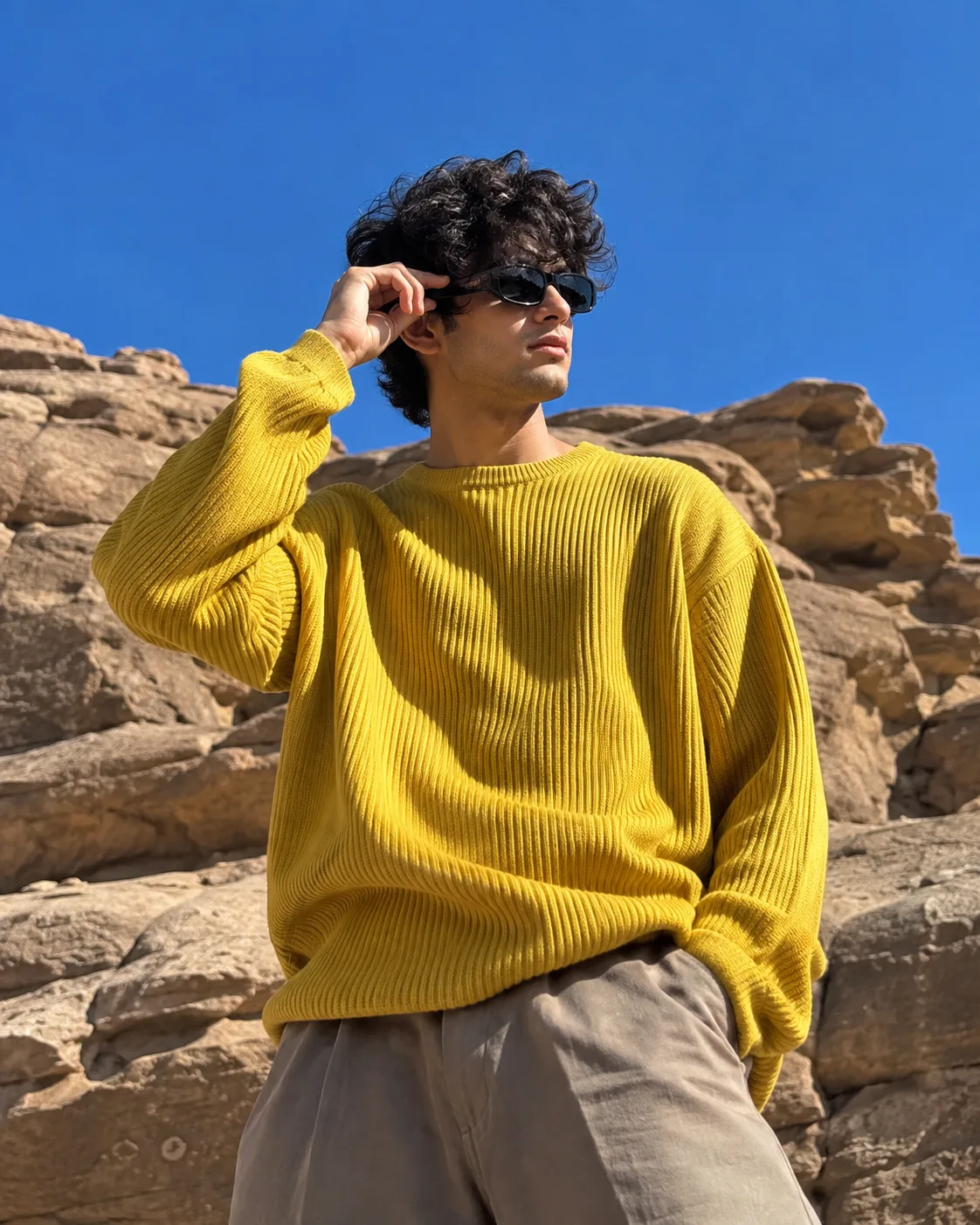 Ultra-realistic outdoor fashion portrait of a young man standing in front of large natural sandstone rock formations under a completely