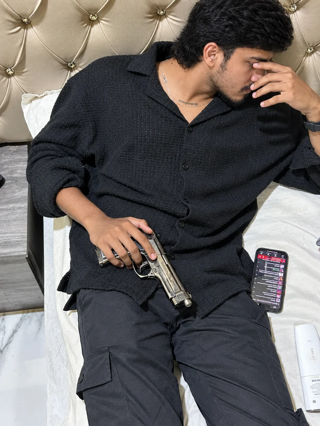 A realistic high-resolution indoor portrait of a young South Asian man reclining diagonally on a bed against a luxurious beige