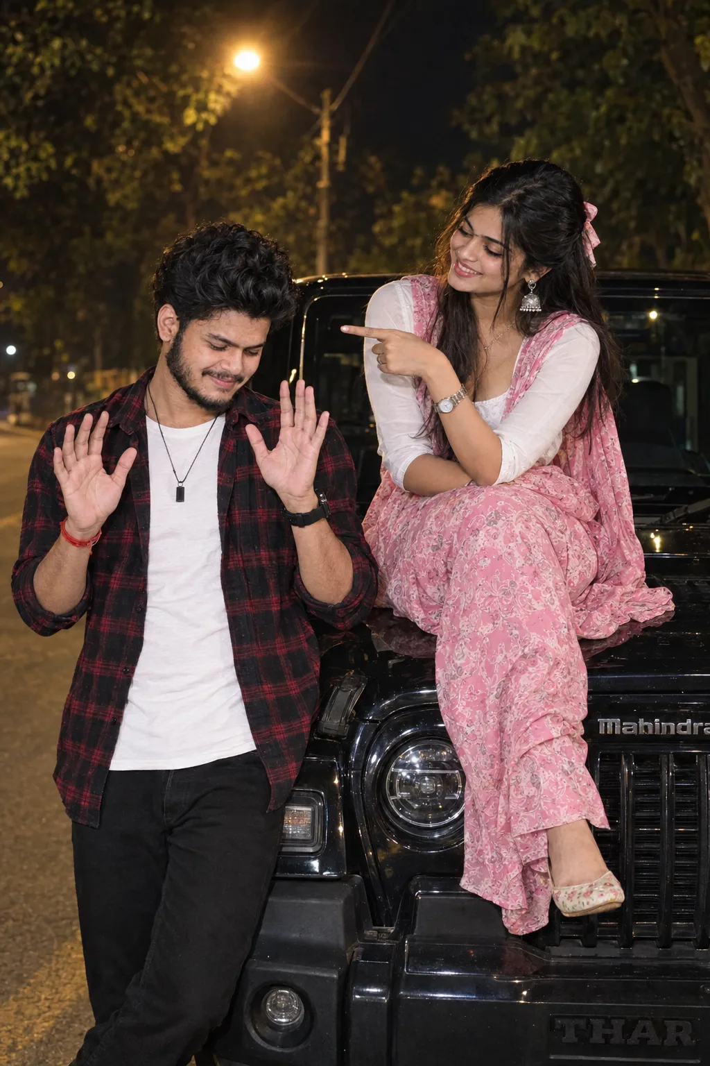 A young Indian man with curly dark hair, light beard and stubble, wearing an open red-and-black plaid flannel shirt over a white t-shirt,