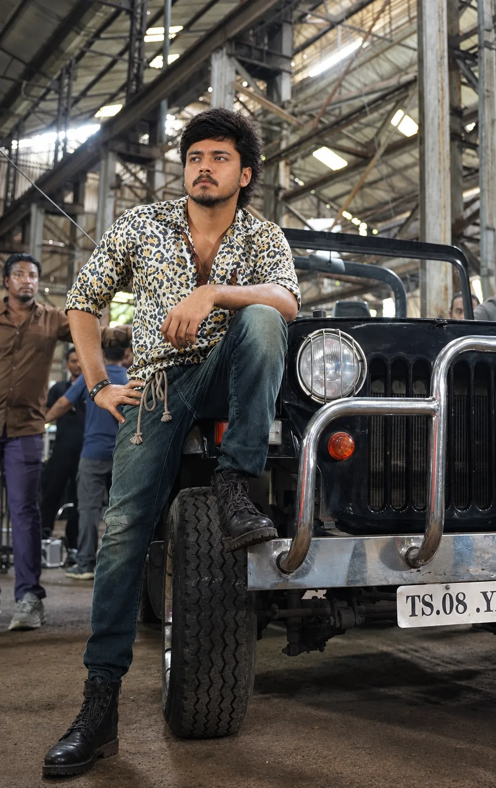 Create a highly realistic cinematic portrait of a young man posing confidently beside a rugged black open-top jeep inside a large