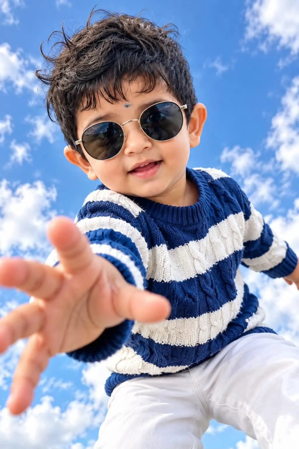 Here is a short prompt for the image: A wide-angle, low-perspective photograph of a young Indian boy wearing round sunglasses and a striped