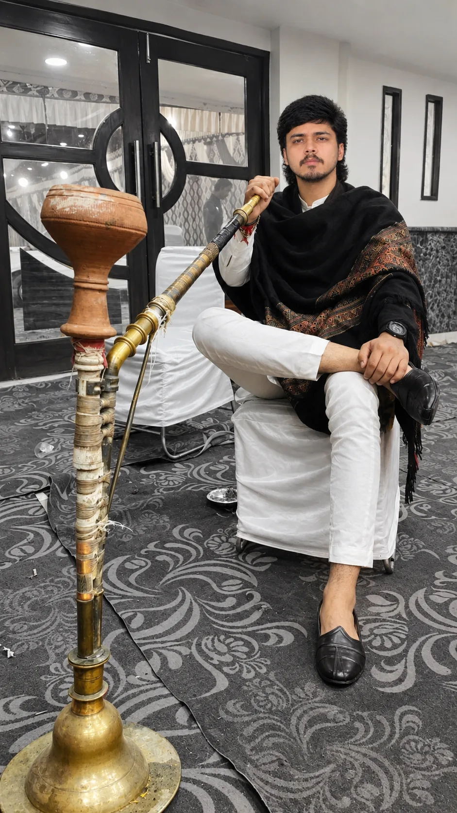 Create a photorealistic cinematic portrait of a young Indian man seated confidently on a white-covered chair in an elegant indoor setting.