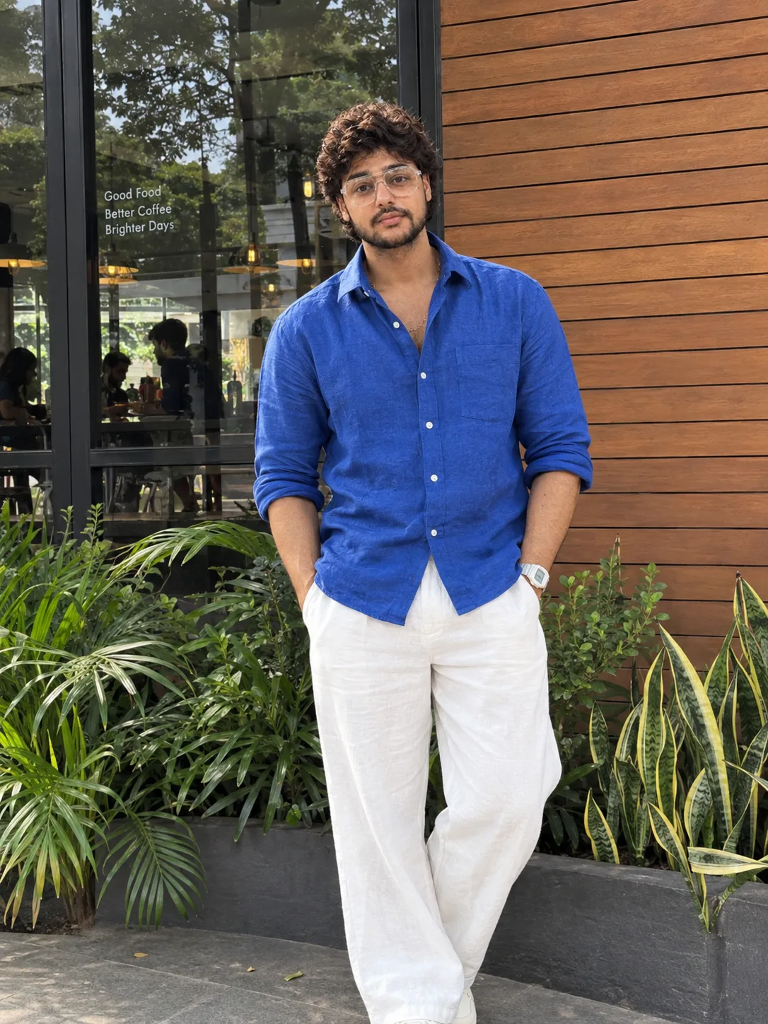 "A clean, candid lifestyle portrait of a young man with thick, tight black curly hair in a short, rounded crop, smiling softly with a calm,