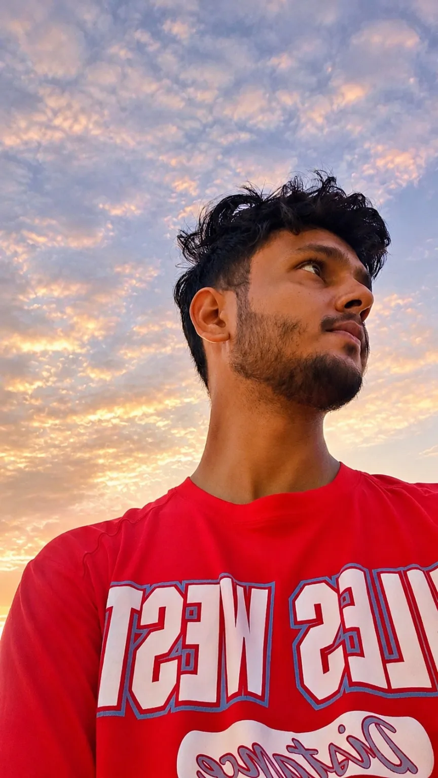 Create a highly realistic, cinematic extreme low-angle outdoor portrait of a stylish young Indian man, photographed from near ground level